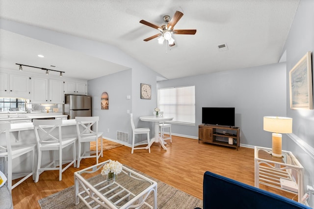 living room featuring visible vents, ceiling fan, light wood finished floors, and vaulted ceiling