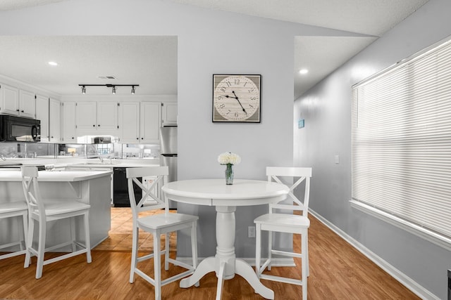 dining space with light wood finished floors, a textured ceiling, track lighting, and baseboards