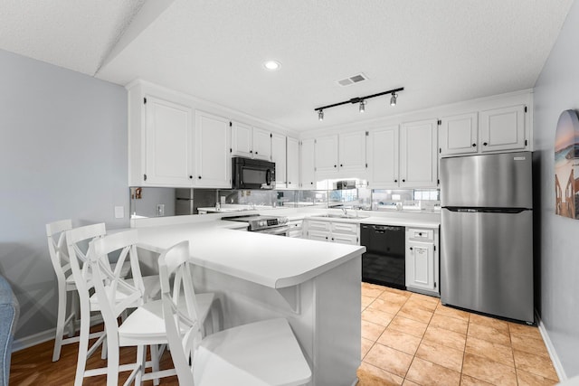 kitchen featuring white cabinets, a sink, light countertops, black appliances, and a peninsula