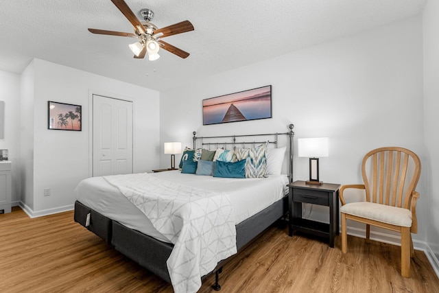bedroom featuring light wood-style floors, a closet, ceiling fan, baseboards, and a textured ceiling