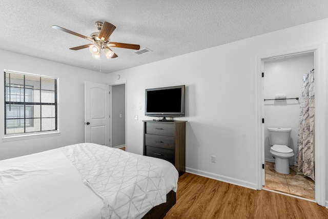 bedroom with a textured ceiling, visible vents, wood finished floors, and ensuite bath