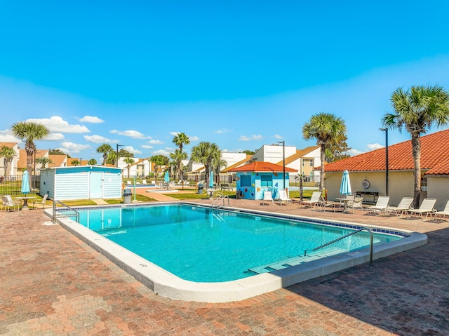 pool with fence, a patio area, a residential view, and an outbuilding