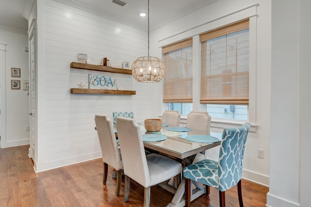 dining area featuring wood-type flooring, ornamental molding, and an inviting chandelier