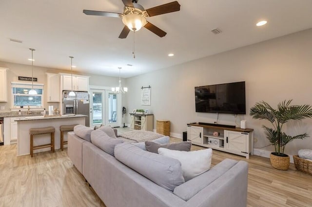 living room with a wealth of natural light, light wood-type flooring, and ceiling fan with notable chandelier