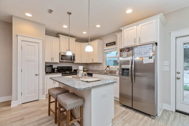 kitchen featuring a kitchen island, hanging light fixtures, white cabinets, light wood-type flooring, and appliances with stainless steel finishes