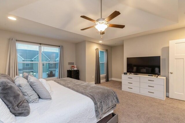 carpeted bedroom with a raised ceiling and ceiling fan