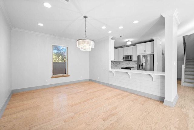 kitchen with kitchen peninsula, white cabinets, appliances with stainless steel finishes, light wood-type flooring, and ornamental molding