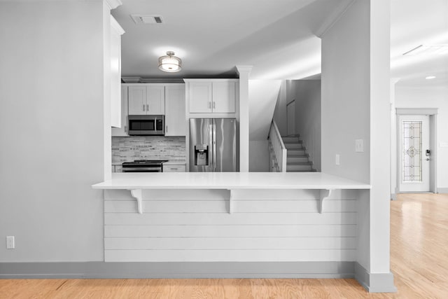 kitchen with backsplash, light hardwood / wood-style floors, stainless steel appliances, crown molding, and a breakfast bar area