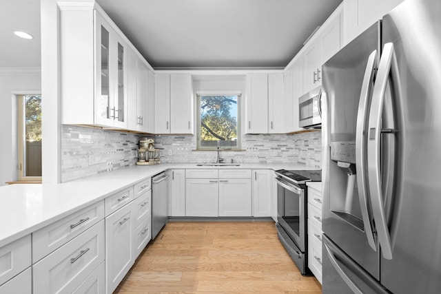 kitchen with decorative backsplash, stainless steel appliances, sink, white cabinetry, and light hardwood / wood-style floors