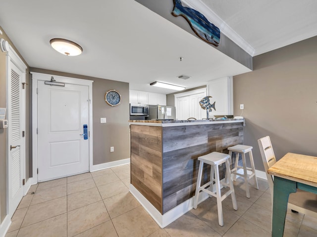 kitchen featuring kitchen peninsula, white cabinets, light tile patterned floors, appliances with stainless steel finishes, and a kitchen breakfast bar