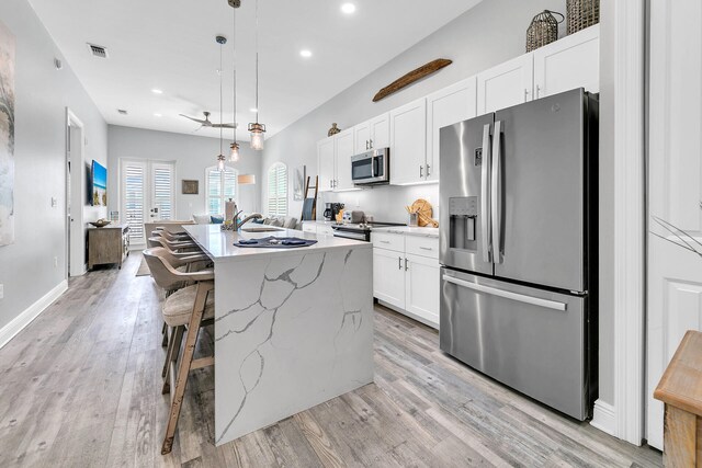 kitchen featuring white cabinets, a center island with sink, a breakfast bar area, pendant lighting, and stainless steel appliances