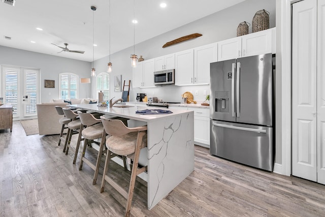 kitchen featuring white cabinets, hanging light fixtures, a kitchen island with sink, a kitchen bar, and stainless steel appliances