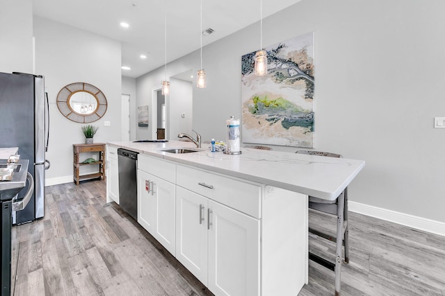 kitchen featuring light stone countertops, appliances with stainless steel finishes, white cabinetry, pendant lighting, and a center island with sink