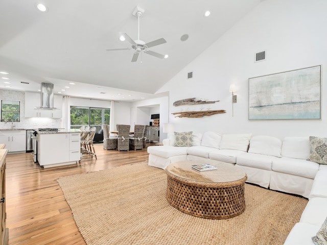 living room with light hardwood / wood-style floors, high vaulted ceiling, sink, and ceiling fan