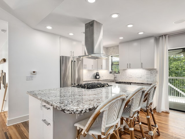 kitchen with a kitchen island, island range hood, a healthy amount of sunlight, and high quality fridge