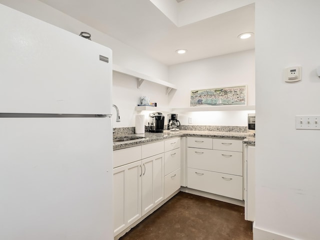 kitchen with light stone countertops, sink, white fridge, and white cabinetry