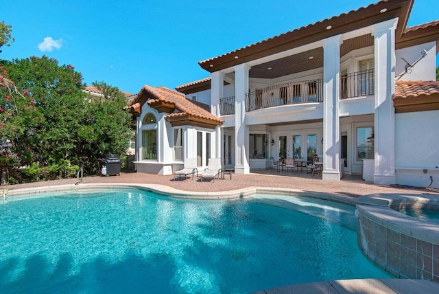 back of house with a patio area, a balcony, and a swimming pool with hot tub