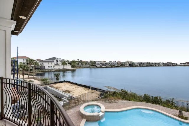 balcony with a water view, an in ground hot tub, and a patio area