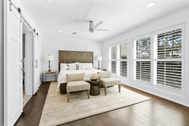 bedroom with ceiling fan, dark hardwood / wood-style floors, and a barn door