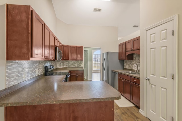 kitchen featuring kitchen peninsula, backsplash, wood-type flooring, sink, and stainless steel appliances