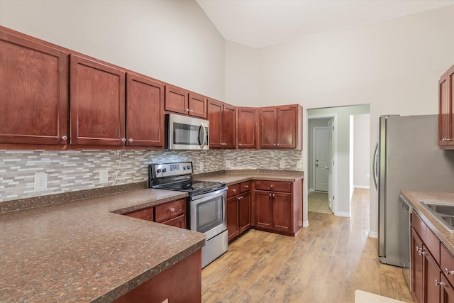 kitchen with backsplash, high vaulted ceiling, appliances with stainless steel finishes, and light hardwood / wood-style flooring