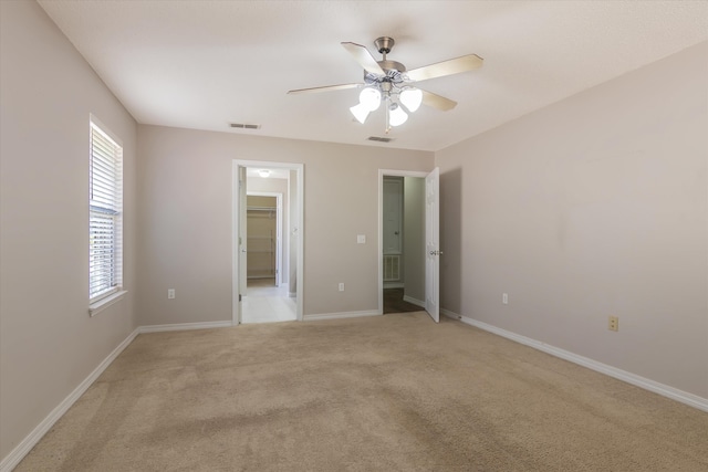 unfurnished bedroom featuring light colored carpet, ceiling fan, a closet, and a walk in closet