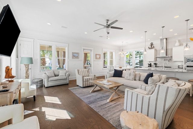 living room featuring crown molding, a healthy amount of sunlight, ceiling fan with notable chandelier, and dark hardwood / wood-style flooring