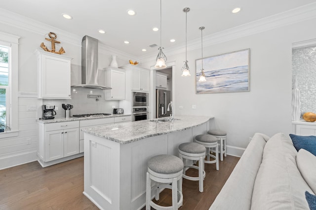 kitchen with white cabinetry, stainless steel appliances, wall chimney exhaust hood, and hanging light fixtures