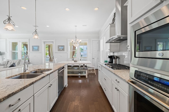 kitchen with sink, stainless steel appliances, wall chimney exhaust hood, pendant lighting, and light stone counters