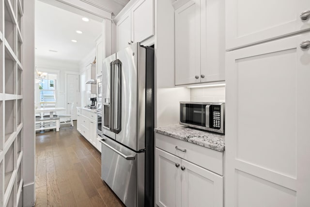 kitchen with dark hardwood / wood-style floors, stainless steel appliances, ornamental molding, white cabinets, and light stone counters