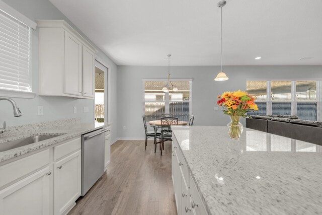 kitchen with white cabinets, stainless steel dishwasher, hanging light fixtures, and light wood-type flooring