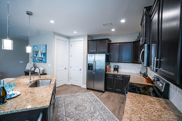 kitchen with stainless steel appliances, sink, light stone countertops, pendant lighting, and light hardwood / wood-style floors