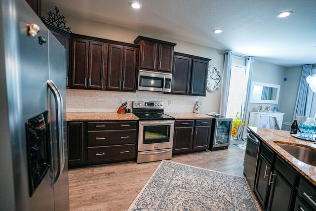 kitchen with stainless steel appliances, sink, light stone counters, a textured ceiling, and light hardwood / wood-style floors