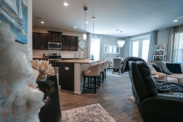 kitchen featuring a center island with sink, a breakfast bar, dark hardwood / wood-style floors, dark brown cabinetry, and decorative light fixtures