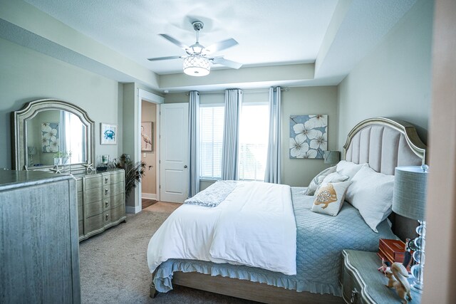 bedroom with ceiling fan, a raised ceiling, and light colored carpet