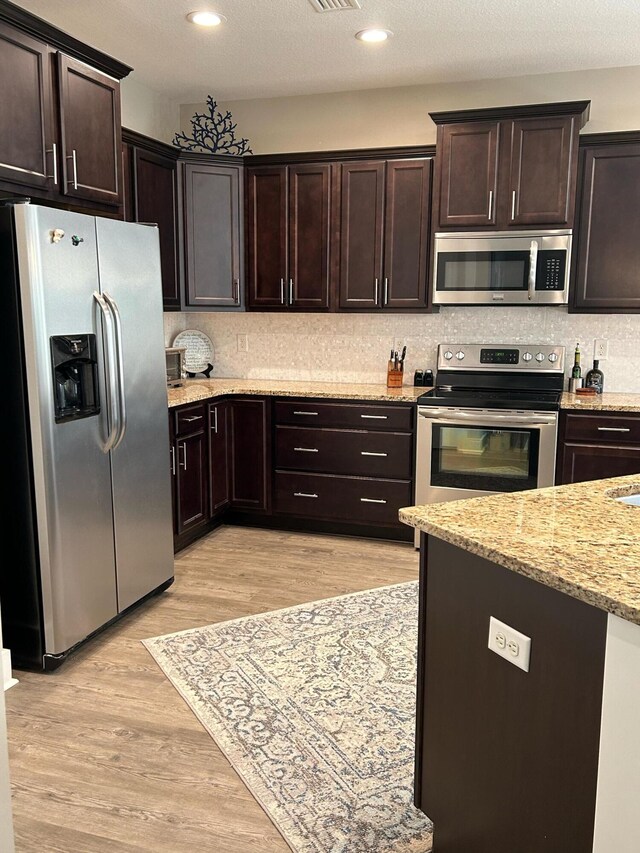 kitchen with light hardwood / wood-style flooring, dark brown cabinets, backsplash, appliances with stainless steel finishes, and light stone counters