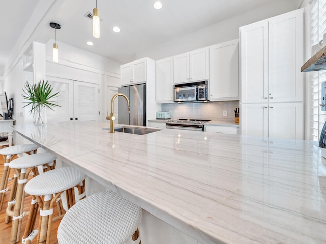 kitchen with hanging light fixtures, stainless steel appliances, sink, light wood-type flooring, and light stone counters