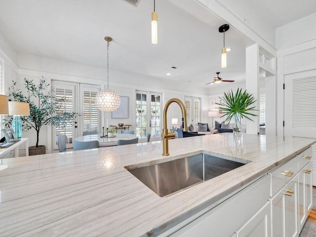 kitchen with light stone countertops, sink, ceiling fan, decorative light fixtures, and white cabinets