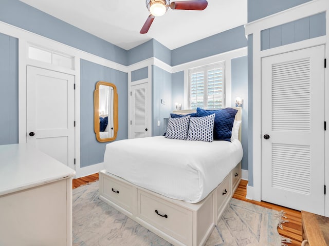 bedroom with two closets, light wood-type flooring, and ceiling fan