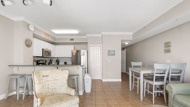 kitchen featuring stainless steel appliances, backsplash, crown molding, light tile patterned flooring, and white cabinets