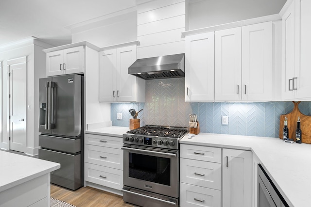 kitchen featuring wall chimney range hood, white cabinets, premium appliances, and backsplash