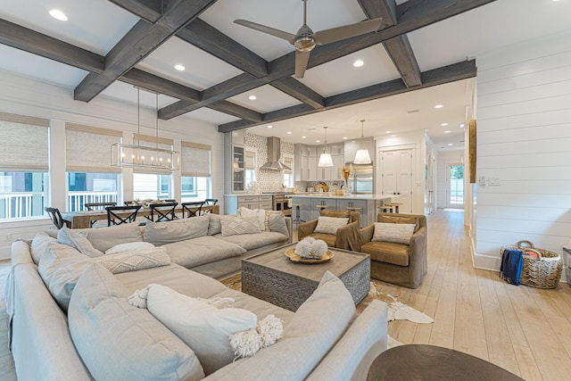 living room featuring wood walls, light wood-type flooring, ceiling fan with notable chandelier, coffered ceiling, and beamed ceiling