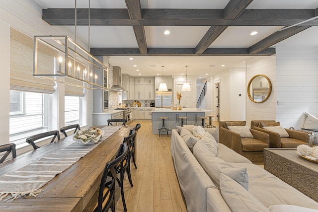 dining space featuring beam ceiling, a chandelier, light wood-type flooring, wooden walls, and coffered ceiling