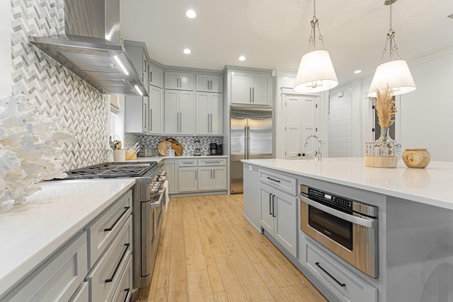 kitchen with light hardwood / wood-style flooring, gray cabinetry, wall chimney exhaust hood, decorative light fixtures, and high end appliances