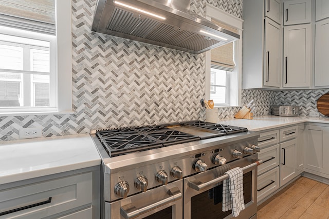 kitchen with range with two ovens, backsplash, light hardwood / wood-style floors, gray cabinets, and premium range hood