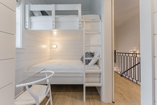 bedroom featuring breakfast area, hardwood / wood-style flooring, and wooden walls