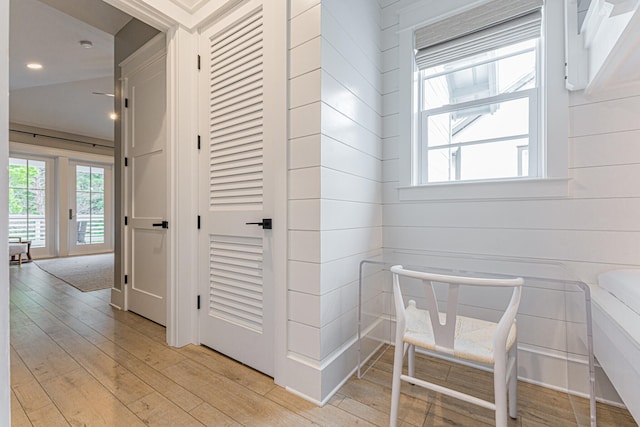 hallway with light hardwood / wood-style floors, wood walls, and vaulted ceiling