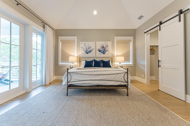 bedroom with access to outside, lofted ceiling, a barn door, and light hardwood / wood-style floors