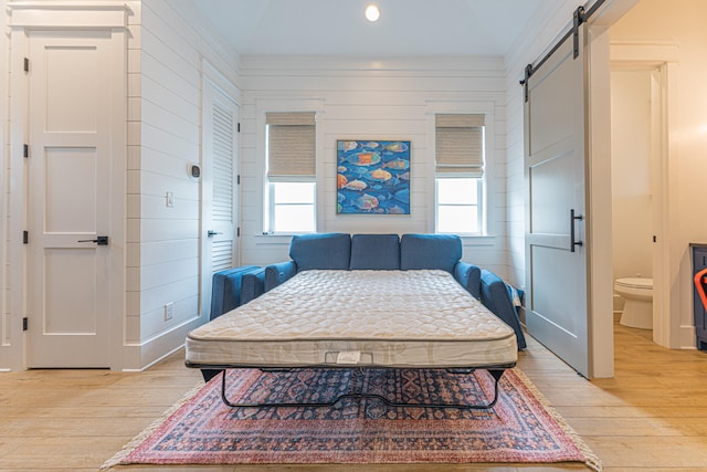 bedroom with light hardwood / wood-style floors, multiple windows, and a barn door