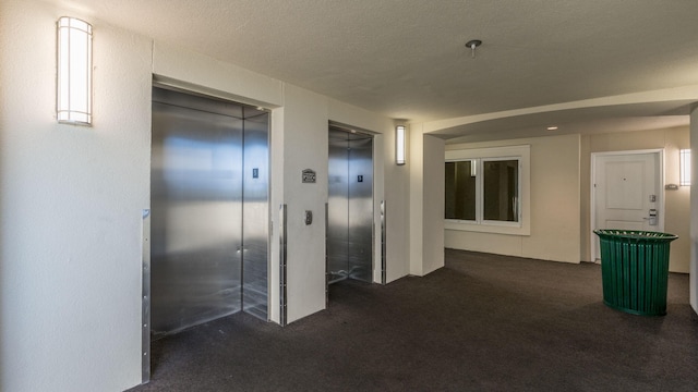 hall featuring elevator, dark colored carpet, and a textured ceiling